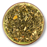 Eine Teeschale mit dem Trockenprodukt des Lavendelbrise Bio, bestehend aus grünem Tee, Lavendelblüten und Zitrusschalen, arrangiert neben einer Tasse frisch aufgebrühten, goldgelben Tees