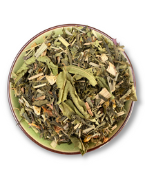 Eine Teeschale mit dem Trockenprodukt des Mango Mojito Bio, bestehend aus grünem Tee, Mangostücken, Pfefferminzblättern und Zitrusschalen, arrangiert neben einer Tasse frisch aufgebrühten, hellgrünen Tees.