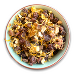 Eine Teeschale mit dem Trockenprodukt des Früchtetees 'Von der Sonne geküsst Bio', bestehend aus Weinbeeren, Mangostücken, Orangenschalen und Ringelblumen
